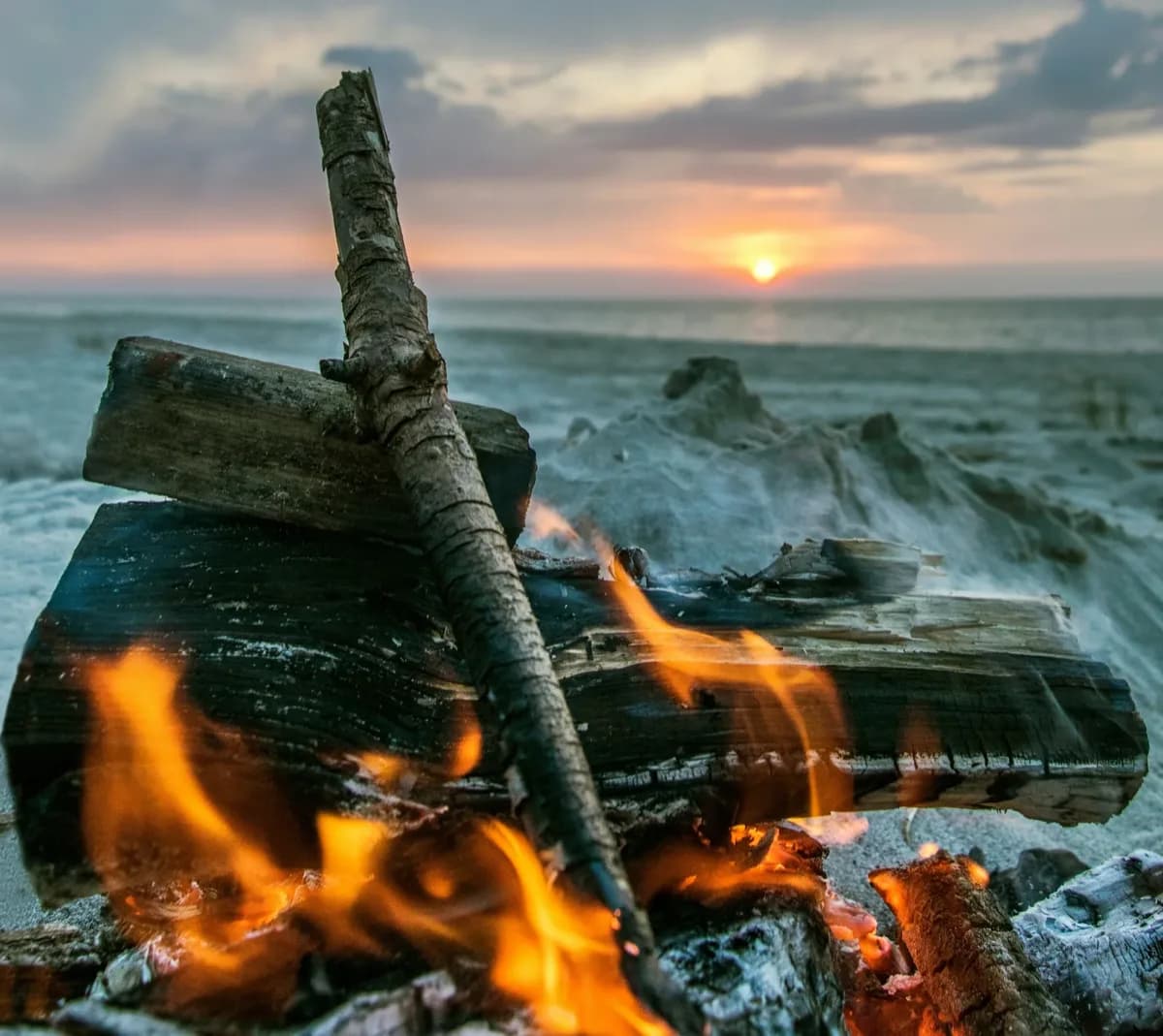A driftwood fire burning on a beach at sunset, the sea stretching toward the horizon